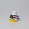 Stack of colorful books with a white cup on a gray background