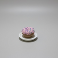 Pink donut with sprinkles on a white plate on a grey surface