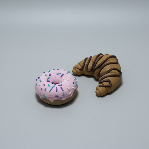 Pink donut with sprinkles and brown croissant magnets on a grey surface