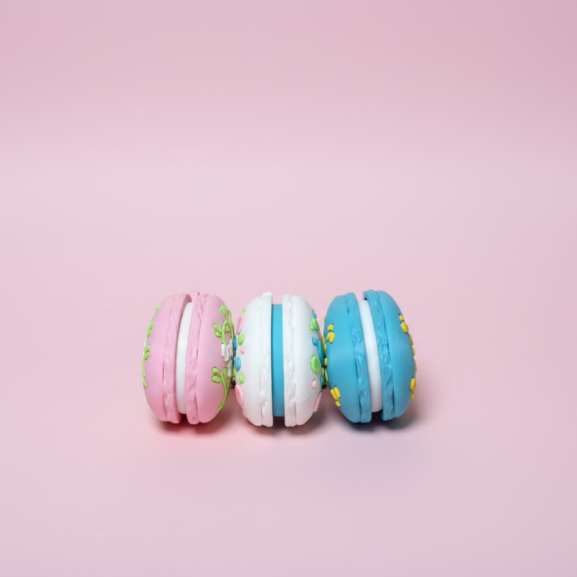 Three macaron-shaped cookies with colorful decorations on a wooden surface