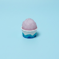 Purple shaved ice in a white cup on a wooden surface